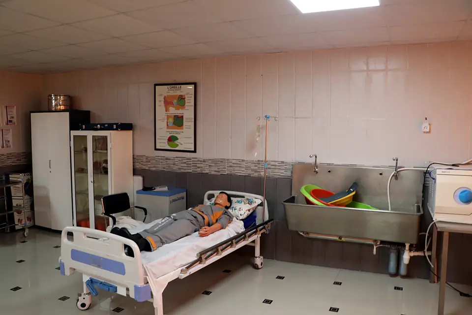 Salle de travaux pratiques avec mannequin sur lit et poste de lavage
